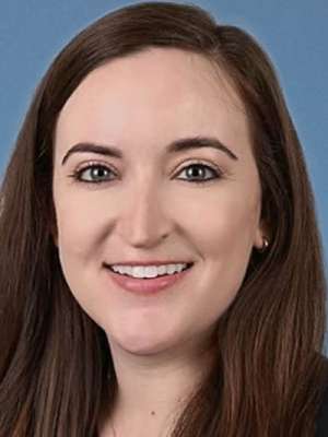 Smiling woman headshot, long brown hair, blue background.