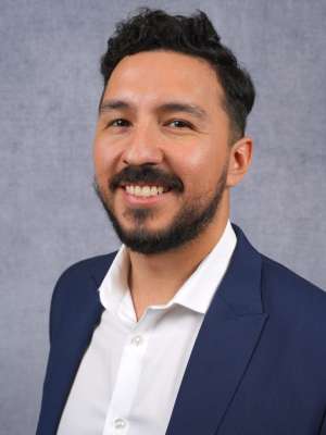 Brian Soto: Smiling with dark hair and trimmed beard wearing navy blazer and white shirt