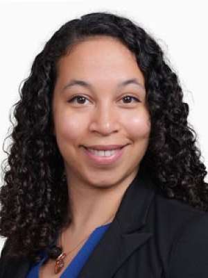 Smiling professional headshot of a person with curly hair wearing a blazer