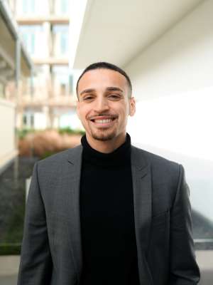 Smiling man in gray blazer and black turtleneck outdoors