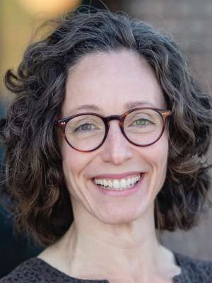Smiling person with curly hair and round glasses, close-up headshot