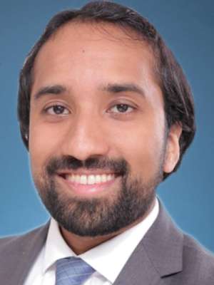 Smiling person in suit and tie headshot on blue background.