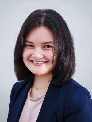 Smiling woman headshot wearing navy blazer and light blouse against pale background