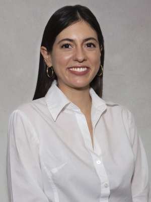 Headshot of woman in white blouse smiling against a neutral gray background.