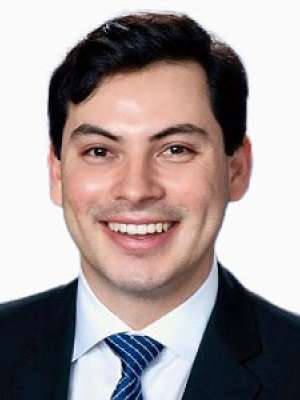 Jordan Juarez smiling headshot in suit and striped tie on white background