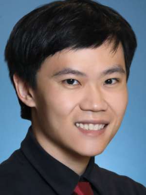 Smiling man headshot in suit and red tie on blue background.