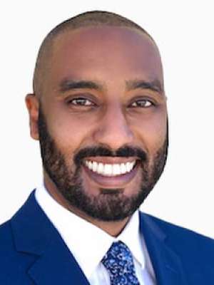Yirgu Brook smiling headshot wearing blue suit and patterned tie