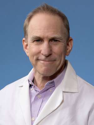 Dr. Yusin, smiling, wearing a white coat against a blue background.