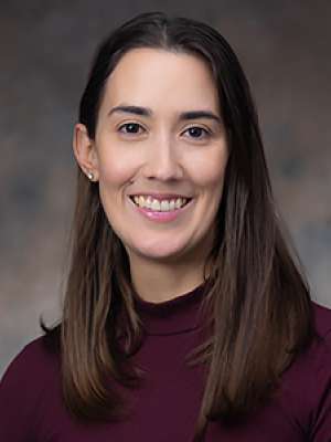 Professional headshot: smiling woman with long dark hair in maroon top