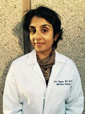 Headshot of a clinician in a white coat and scarf against a textured wall.