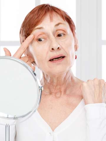 Mature woman with finger on skin looking to the mirror.