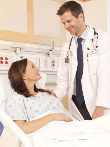 Doctor standing by female patient's bedside smiling