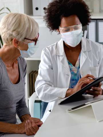 A doctor with a face shield and mask discussing with a masked patient.