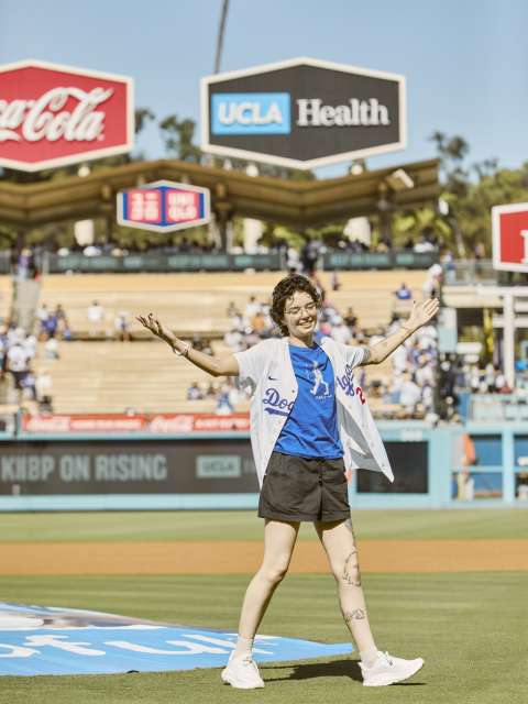 A woman smiles with arms stretched wide as she walks off the field at Dodger Stadium