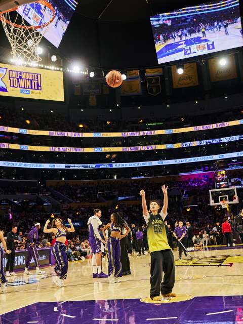 A teen girl shoots a basketball on the Los Angeles Lakers court.