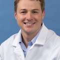 White coat head shot of Brian DeLue, smiling at the camera