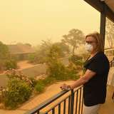 Woman stands on porch looking out at smoke from fire