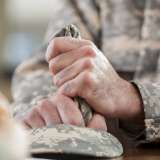 Caucasian male veteran squeezes camouflage uniform hat during counseling session. Close up is of the man holding the hat.