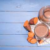 A pitcher and glass of chocolate beverage with sweet potatoes on a checkered cloth.