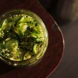 Jar of sliced cucumbers in vinegar on a wooden surface.