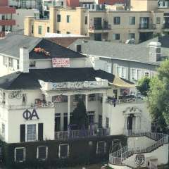 White multi-story house with Greek letters, banners and rooftop graffiti