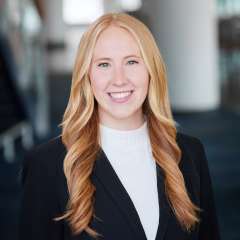 A woman with blonde hair, wearing a white sweater with a suit jacket