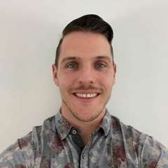 Luke Cunningham wearing a camouflage collared shirt smiling against a white background