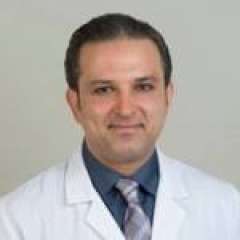 Dr. Mohammad Kamgar, wearing a white medical coat, a dark blue shirt, and a purple tie. His friendly expression conveys a professional and kind demeanor.