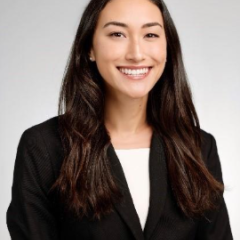 Professional headshot of a woman with long, dark hair, wearing a black blazer.