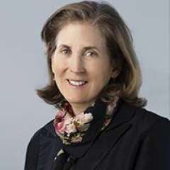 Dr. Judith Currier with brown hair, wearing a black jacket and a patterned scarf. Her direct gaze conveys confidence and approachability.