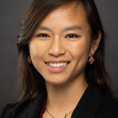 Smiling woman in blazer and necklace against a gray backdrop