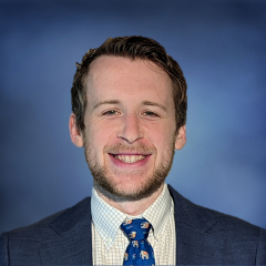 Head shot of Jacob Klickstein in a suit, smiling at the camera