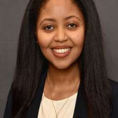 Headshot of Enat wearing a black suit and cream shirt