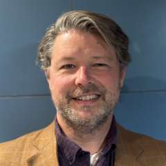 Man in a plaid suit jacket against a blue background.