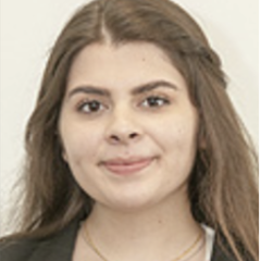Headshot of a person with long brown hair, wearing a blazer and pink top.