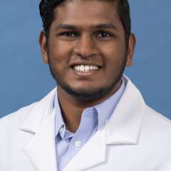 White coat head shot of Roshan Srinivas Srinivasan, smiling at the camera