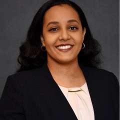 Bethlehem Michael professional headshot. Beth is smiling and wearing a black suit with light pink shirt. 