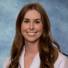 headshot of Dr. Adrienne Leigh in front of a blue background, wearing a lab coat