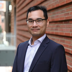 Dr. Neil Lin wearing a dark blue suit and standing against brick wall