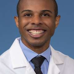 Head shot of Paul Lewis, MD, MS in white coat, smiling at camera