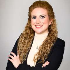Headshot for Catherine Donat in front of a gray background in an indoor setting