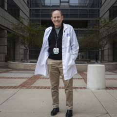 Jeffrey Conklin in white lab coat standing outside with an ID badge