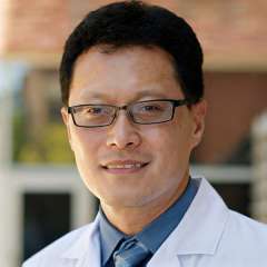 Smiling person in white coat and glasses outdoors