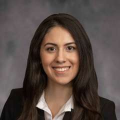 A woman with brown hair, wearing a blazer with a white shirt
