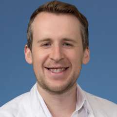 Smiling person in white lab coat and collared shirt on blue background