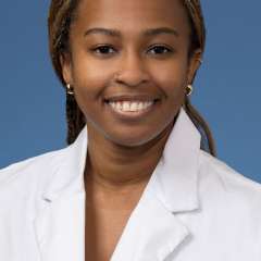 Head shot of Angela Udongwo, MD, MPH, in white coat, smiling at camera