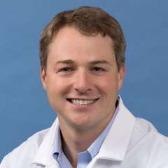 White coat head shot of Brian DeLue, smiling at the camera