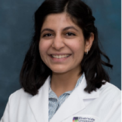 A woman with wavy black hair, wearing a resident physician's coat