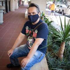 Petur Leosson wearing a dark face mask seated on a low outdoor ledge beside plants.