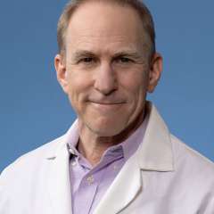 Dr. Yusin, smiling, wearing a white coat against a blue background.